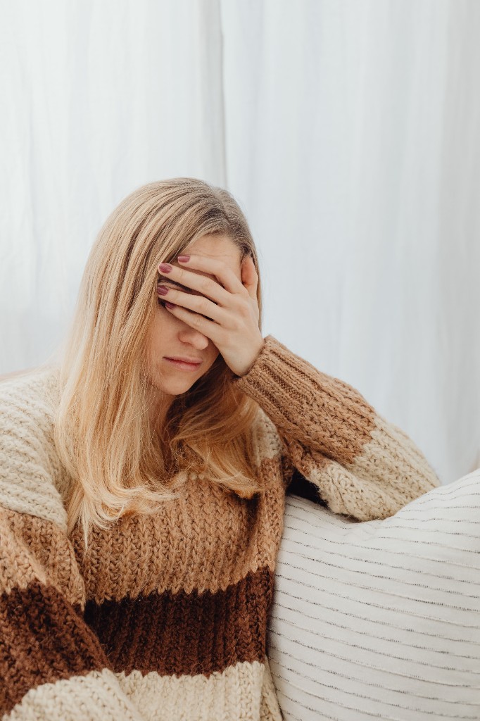 A person sits on a sofa with a hand resting on their forehead